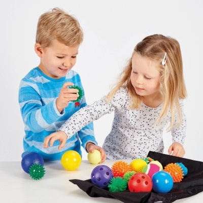 Crianças a brincar com bolas coloridas e texturizadas em frente a uma bolsa preta