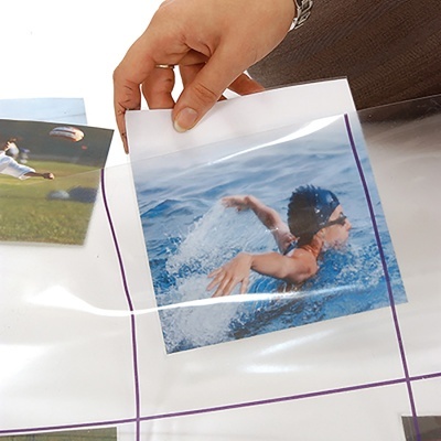 Mão a inserir fotografia num bolso plástico transparente com linhas roxas em folha transparente