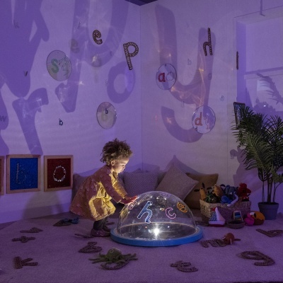 Criança a brincar com dispositivo de luz em quarto decorado com letras e plantas