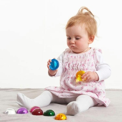 Bebé sentada com vestido rosa e brinquedos coloridos