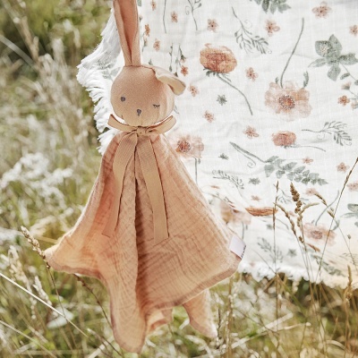 Peluche coelho castanho claro com tecido salmão pendurado junto a pano floral branco ao ar livre