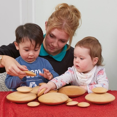 Discos de madeira naturais em várias dimensões sobre tecido vermelho com mulher e duas crianças a brincar.