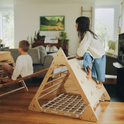 Estrutura triangular de madeira clara para crianças com rede e apoios de escalada em sala de estar