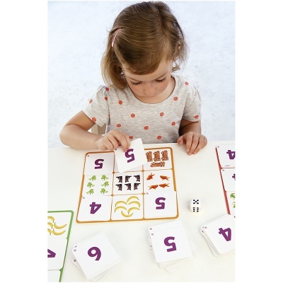 Menina a jogar cartas com números e figuras de animais numa mesa branca