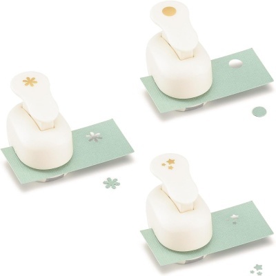 Três perfuradores de papel brancos com detalhes de corte em formas de flores e círculos sobre base verde
