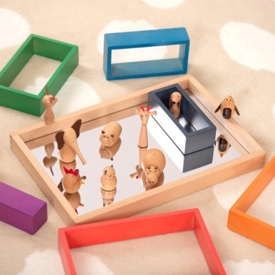 Bandeja de madeira com espelho e miniaturas de animais de madeira ao centro, rodeada por blocos retangulares coloridos.