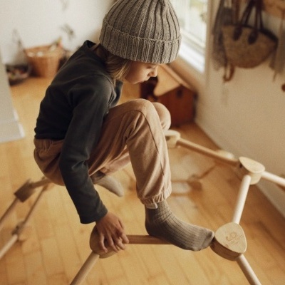 Criança com roupa neutra sentada numa estrutura de madeira clara em ambiente interior com chão de madeira