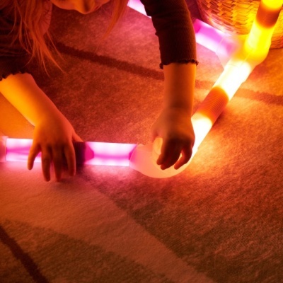 Criança a montar tubos luminosos flexíveis rosa e laranja no chão