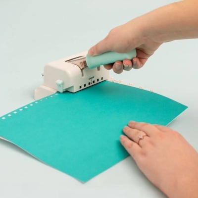 Máquina de perfuração manual branca com pega azul clara a furar papel azul
