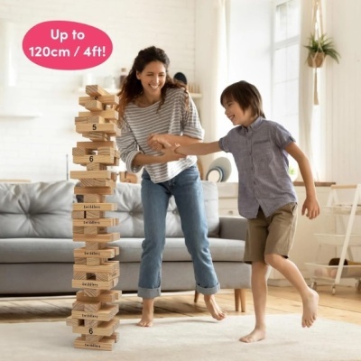 Torre alta de blocos de madeira naturais com números e palavras, crianças brincando numa sala iluminada