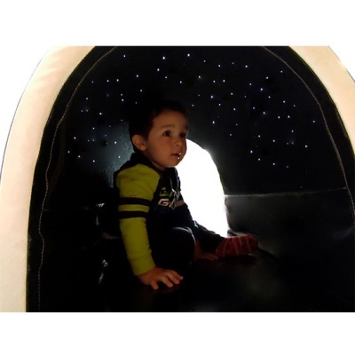 Tenda preta com luzes simulando estrelas e criança sentada no interior