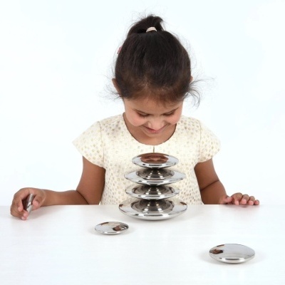 Menina olhando para discos metálicos prateados empilhados num fundo branco