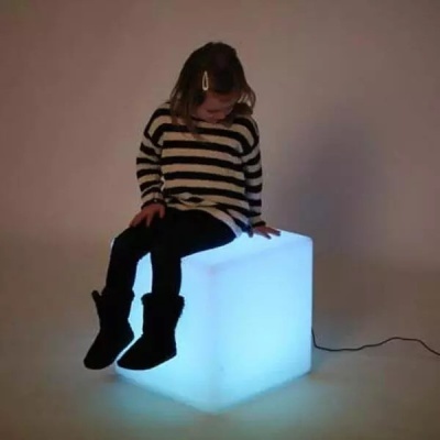 Menina sentada num cubo luminoso branco a brilhar num fundo neutro