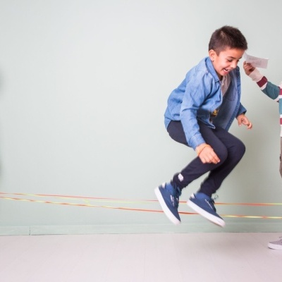 Crianças brincando com elásticos coloridos dentro de uma sala de parede verde claro