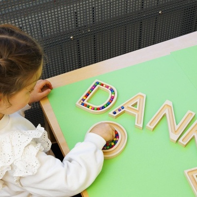Criança montando letras de madeira coloridas sobre fundo verde formando a palavra DANKE