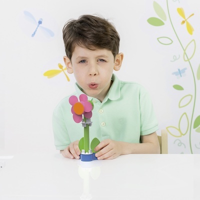 Menino com camiseta polo verde claro segurando flor de brinquedo colorida sentado à mesa branca