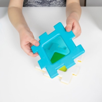 Peça de plástico azul com buraco triangular a ser encaixada numa base branca por uma criança.