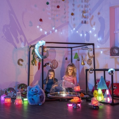 Duas crianças em brinquedos iluminados dentro de estrutura quadrada preta com decoração colorida