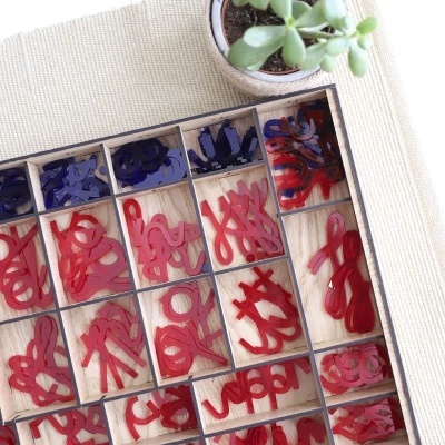 Caixa com letras vermelhas e azuis em acrílico e planta suculenta num vaso branco