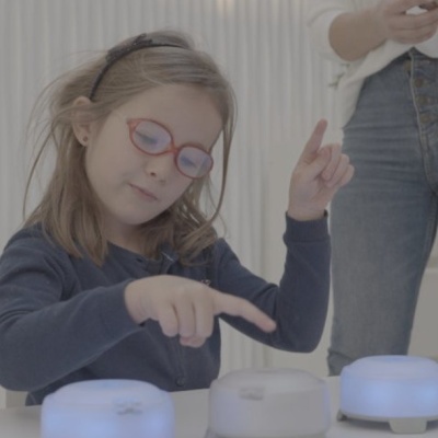 Criança a interagir com dispositivos eletrónicos brancos iluminados numa mesa branca