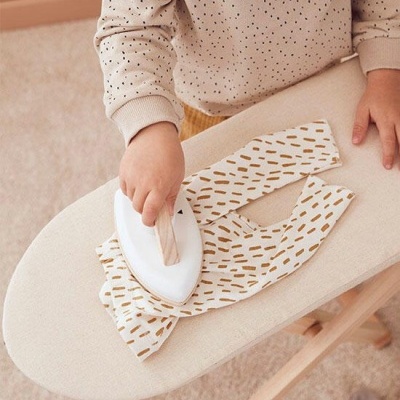 Criança passando ferro em roupa branca com padrão castanho claro na tábua de engomar