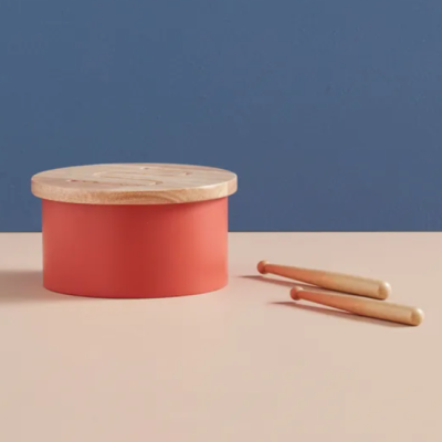 Tambor de brinquedo vermelho com tampa de madeira e baquetas numa mesa
