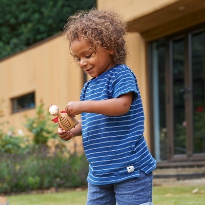 Criança sorridente com roupa azul segurando brinquedo de madeira ao ar livre