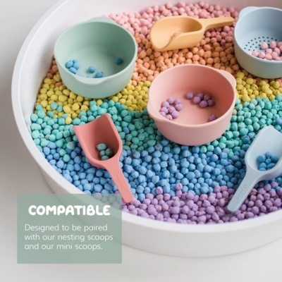 Colheres e taças de plástico coloridas dentro de recipiente branco com esferas coloridas e texto COMPATIBLE em inglês