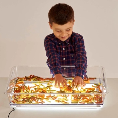 Criança a brincar com massas coloridas num tabuleiro transparente iluminado.