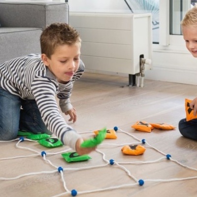 Duas crianças a jogar um jogo de tabuleiro com peças coloridas sobre uma rede no chão