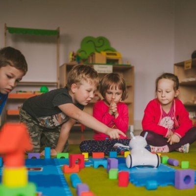 Crianças a brincar com blocos de construção e robô branco num tapete colorido numa sala de aula