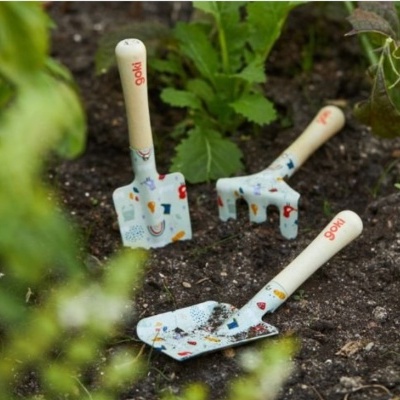 Três ferramentas de jardim infantis coloridas com cabos de madeira em solo de jardim