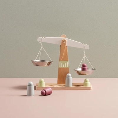 Balança de madeira com peças coloridas sobre superfície rosa