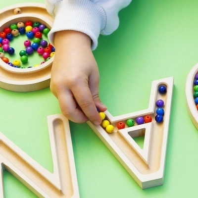 Letras de madeira com contas coloridas dentro, em superfície verde, mão de criança a manipular uma letra.