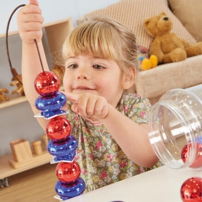 Criança a brincar com brinquedo de contas coloridas numa mesa branca