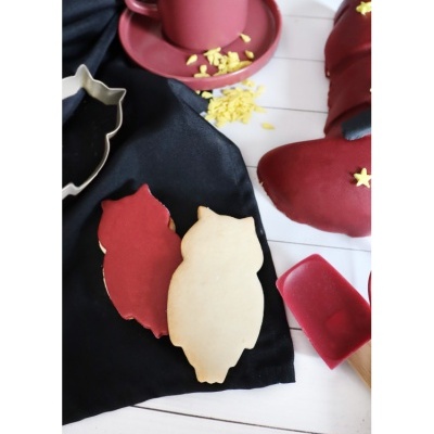 Bolachas em forma de coruja decoradas vermelho e bege com acessórios de cozinha vermelhos e tecido preto