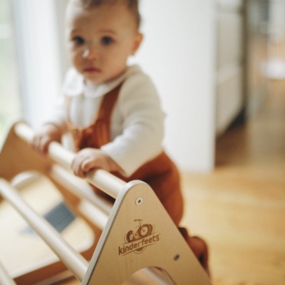 Brinquedo de madeira claro com criança ao fundo, rótulo kinderfeets