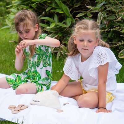 Duas meninas sentadas num tecido branco no relvado com moedas de madeira e saco de tecido
