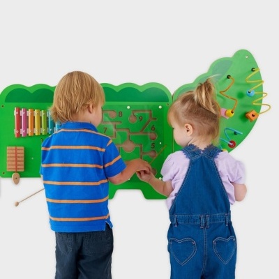 Painel de atividades infantil em madeira verde com números, xilofone e contas coloridas, duas crianças a brincar