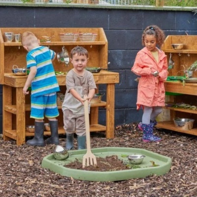 Crianças a brincar com brinquedo de cozinha exterior em madeira com utensílios metálicos.
