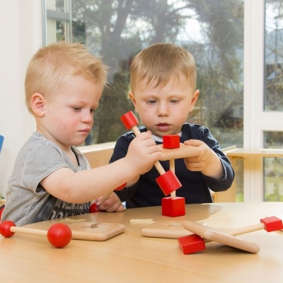 Crianças a brincar com brinquedo de madeira vermelho e natural num espaço iluminado.