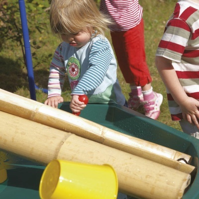 Criança a brincar com brinquedo de água e bambu num parque exterior