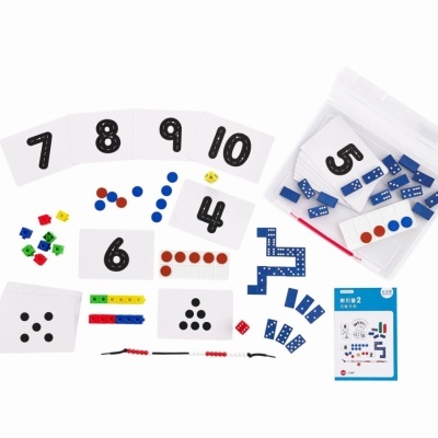 Conjunto de jogo educativo com cartas, fichas coloridas, peças azuis, dados e manual em alemão sobre fundo branco