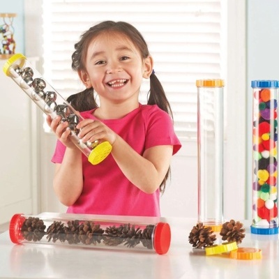 Criança com tubos transparentes contendo bolas metálicas, pinhas e bolas coloridas