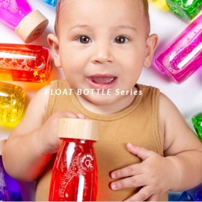 Criança com garrafa vermelha transparente e tampas de madeira entre garrafas coloridas