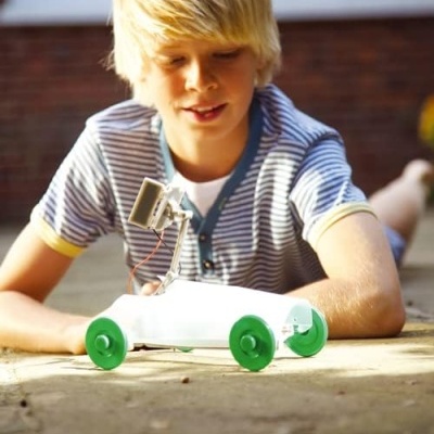 Menino loiro a brincar com carro de brinquedo branco com rodas verdes ao ar livre