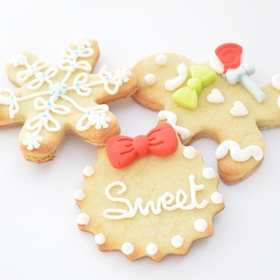 Três biscoitos decorados com glacê colorido, incluindo um floco de neve, um boneco de gengibre e um biscoito redondo com a palavra 'Sweet'.