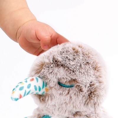 Brinquedo de peluche cinzento com bico com padrão colorido e uma mão de criança a tocar