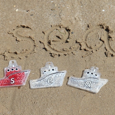 Três brinquedos de barco de plástico com letras s, e, a na areia