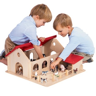 Duas crianças brincam com estábulo de madeira para animais de fazenda com telhado vermelho